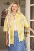 Woman wearing a yellow shirt with blue graphics and a blue skirt, standing in a room.